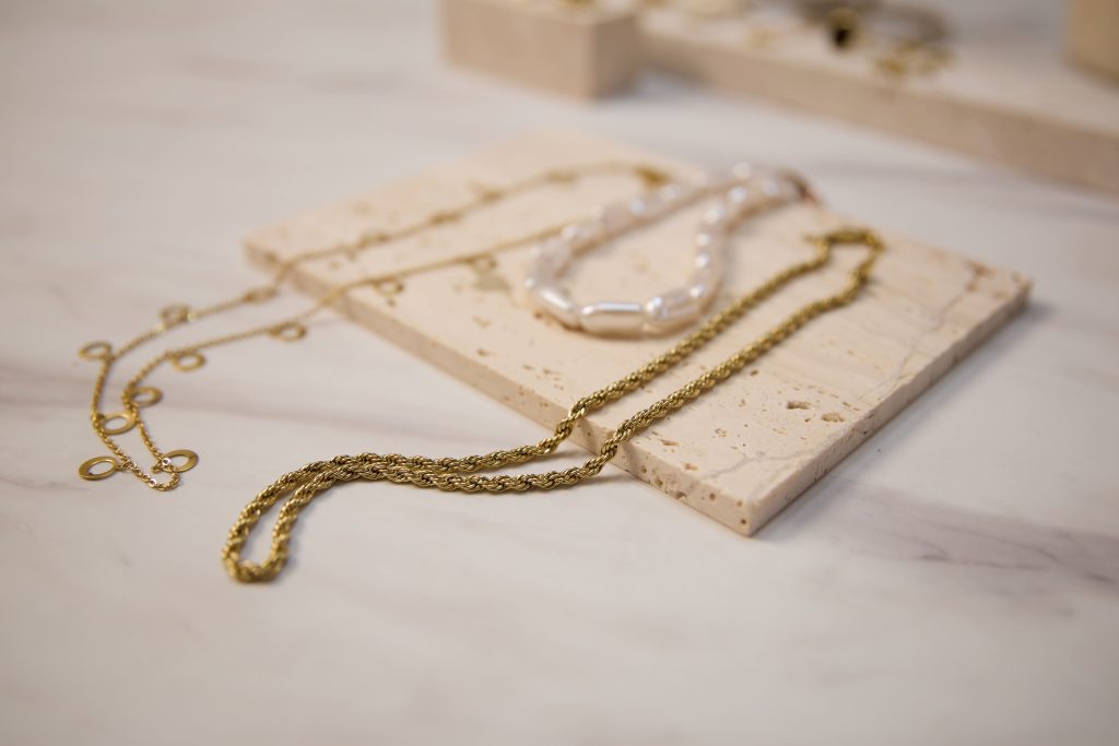 Elegante Halskettendarstellung mit Goldketten & Perlenentwürfen, Gecurrierte Damenhalskettensammlung auf Minimalistischen Travertineständen