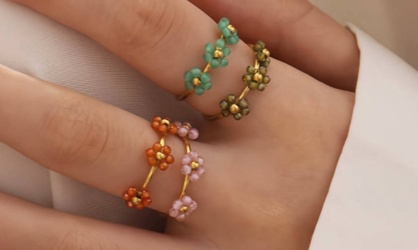 Farverige parelbloemringen (groen, oranje, roze) op een vinger, met gouden accenten voor een verspielde, delicate uitstraling