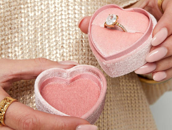 Large stone ring in a pink heart-shaped velvet jewelry box, held by hands with light pink nail polish